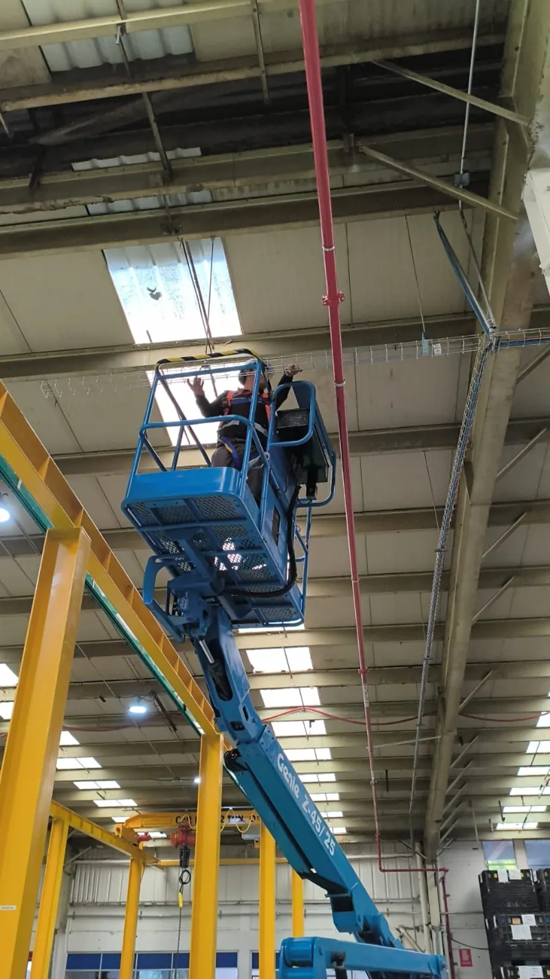 Técnico en plataforma de elevación instalando charola para cableado en una planta
