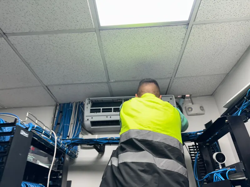 Técnico dando mantenimiento al aire acondicionado de un cuarto de telecomunicaciones
