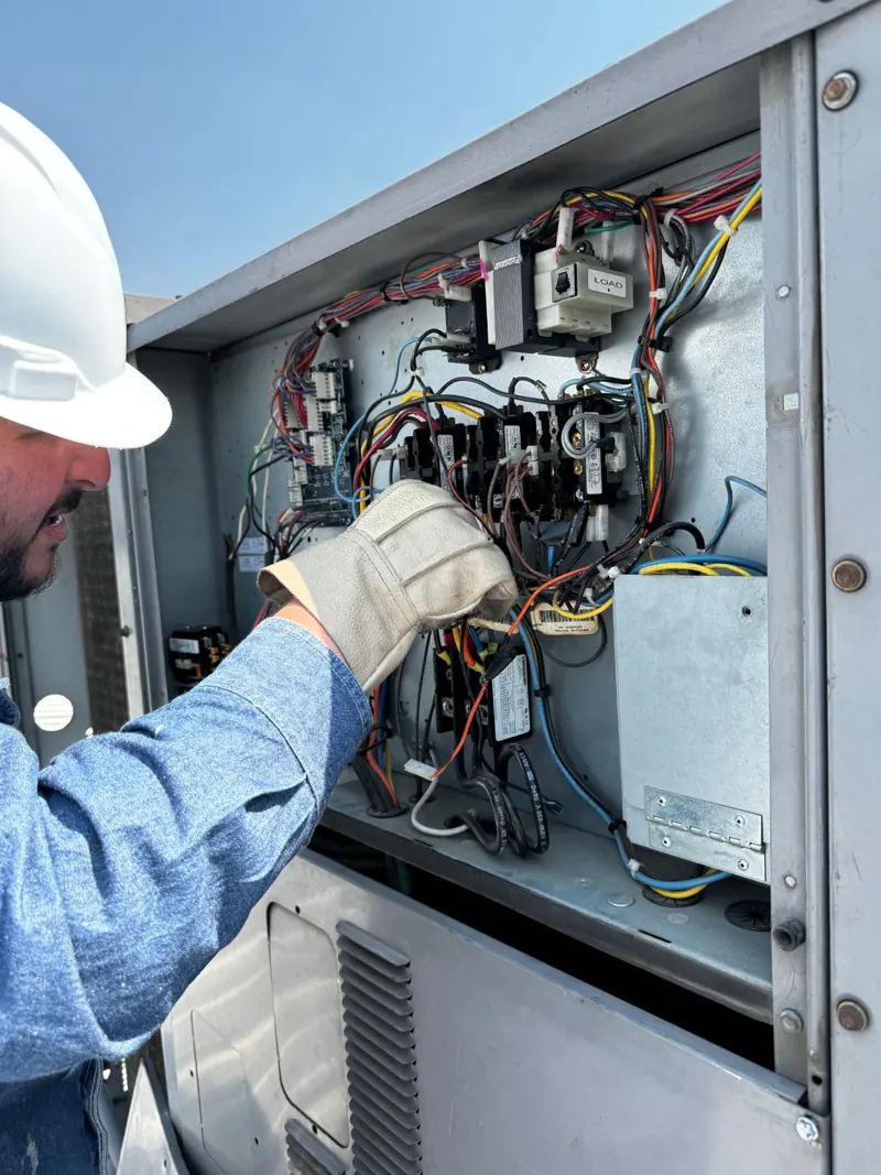 Técnico con casco y guantes revisando el tablero eléctrico de un aire acondicionado